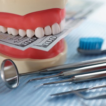 Artificial teeth biting down on $100 bills next to dental instruments