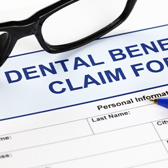 Blue top of dental benefits claim form with black-framed glasses and a pen