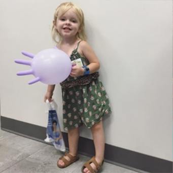 Smiling little girl holding inflaed rubber glove