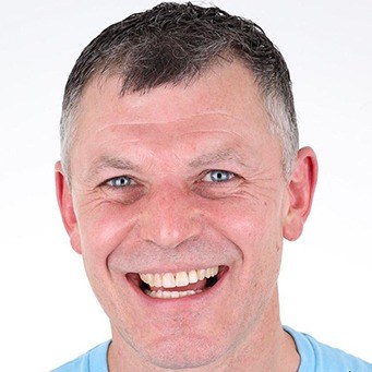 Man with dark and grey hair smiling with white background