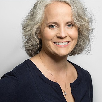 Woman with grey hair and necklace smiling with grey background