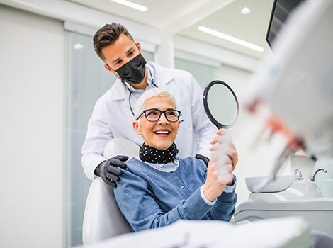 Woman smiling at reflection in handheld mirror with dentist