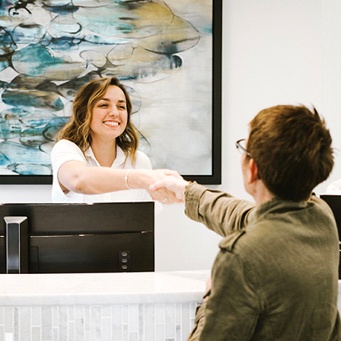 dental team member shaking a patient’s hand over the front desk 