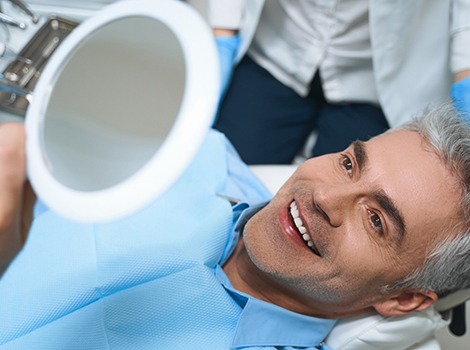 Man with straight teeth smiling at reflection in mirror