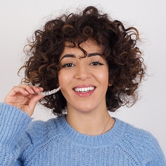 Smiling patient holding clear aligner