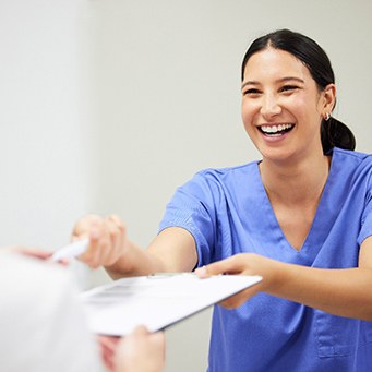 Dental assistant smiling while handing patient form