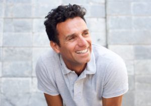 Middle-aged man smiling with dental implants in white shirt