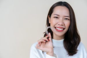 Woman holding Invisalign while smiling at the camera