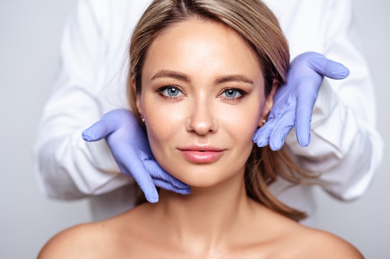 Dentist framing a woman’s face with gloved hands