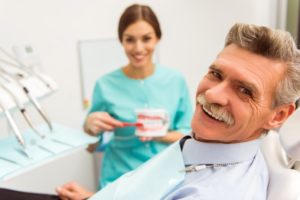 a man smiling with his dentist as she shows him how to care for his dentures