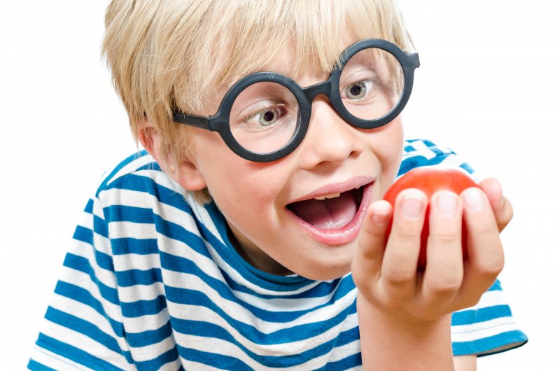A child in glasses about to bite into a tomato