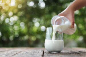 Person pouring a glass of milk against a pastoral background.